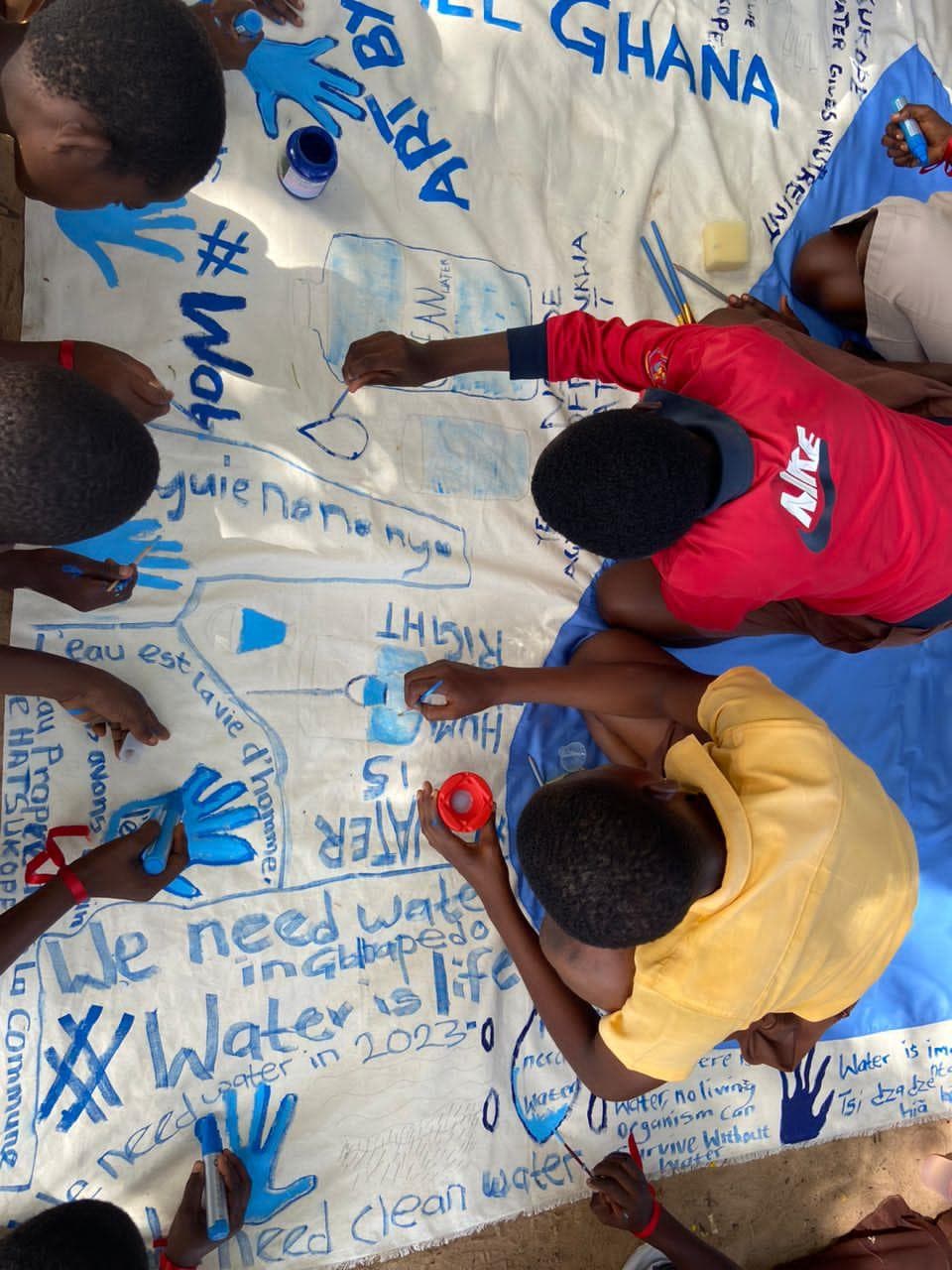 Young people painting a community water-justice banner at an art activation in Ghana